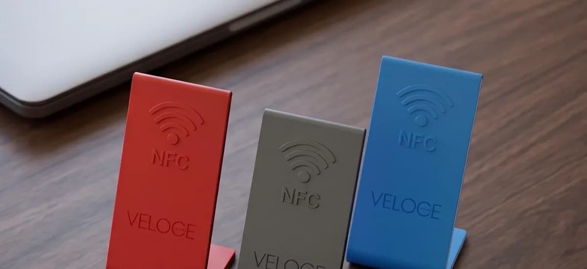 Tres stands NFC de mostrador en rojo, grafito y azul sobre un escritorio